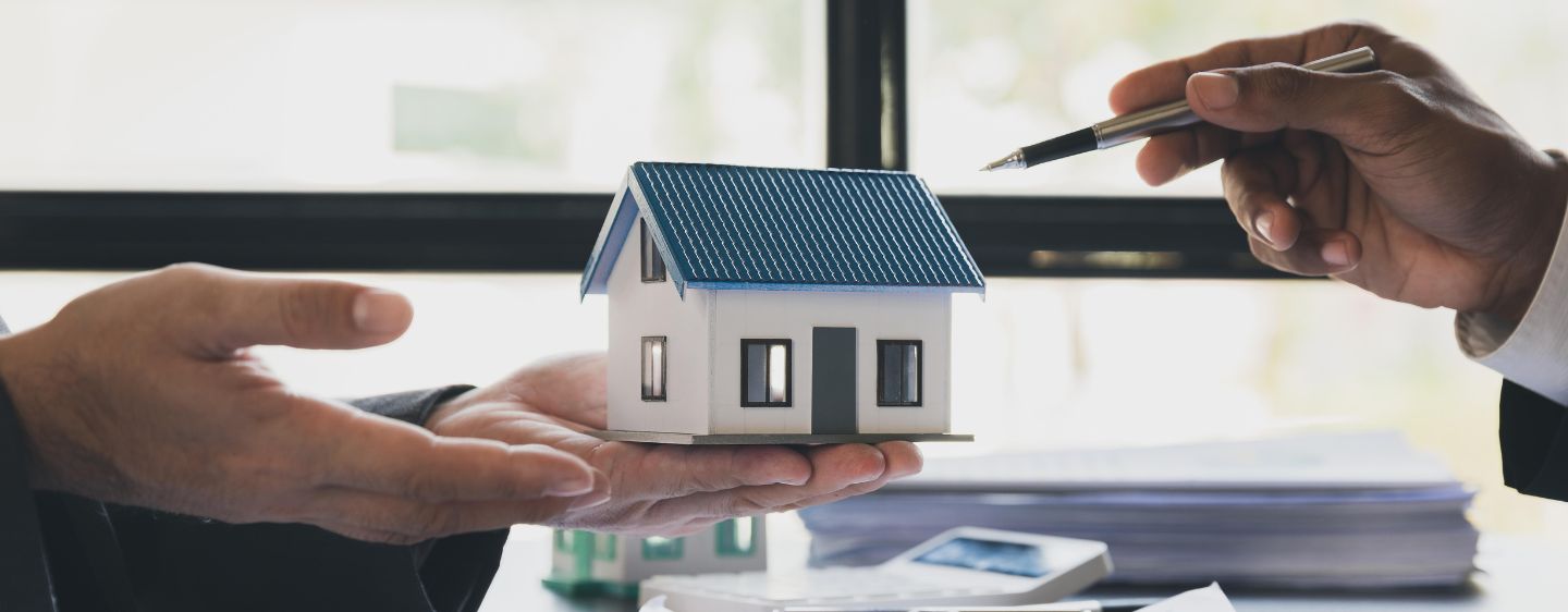 Miniature house with pen pointing to it. 