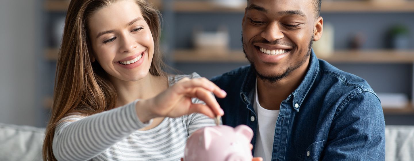 Couple smiling as they put money into a piggy bank.