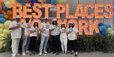 An image of CCU team members in front of a lit up sign that reads Best Places to Work